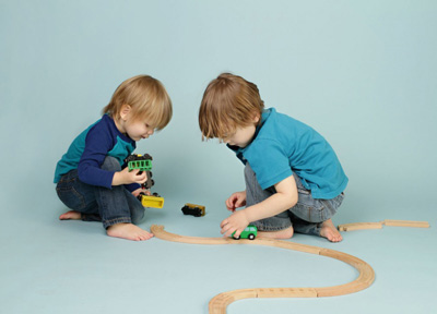Two young boys share a toy train set.